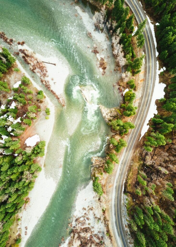 An overhead picture of a riverside with beautiful green woods on both sides.